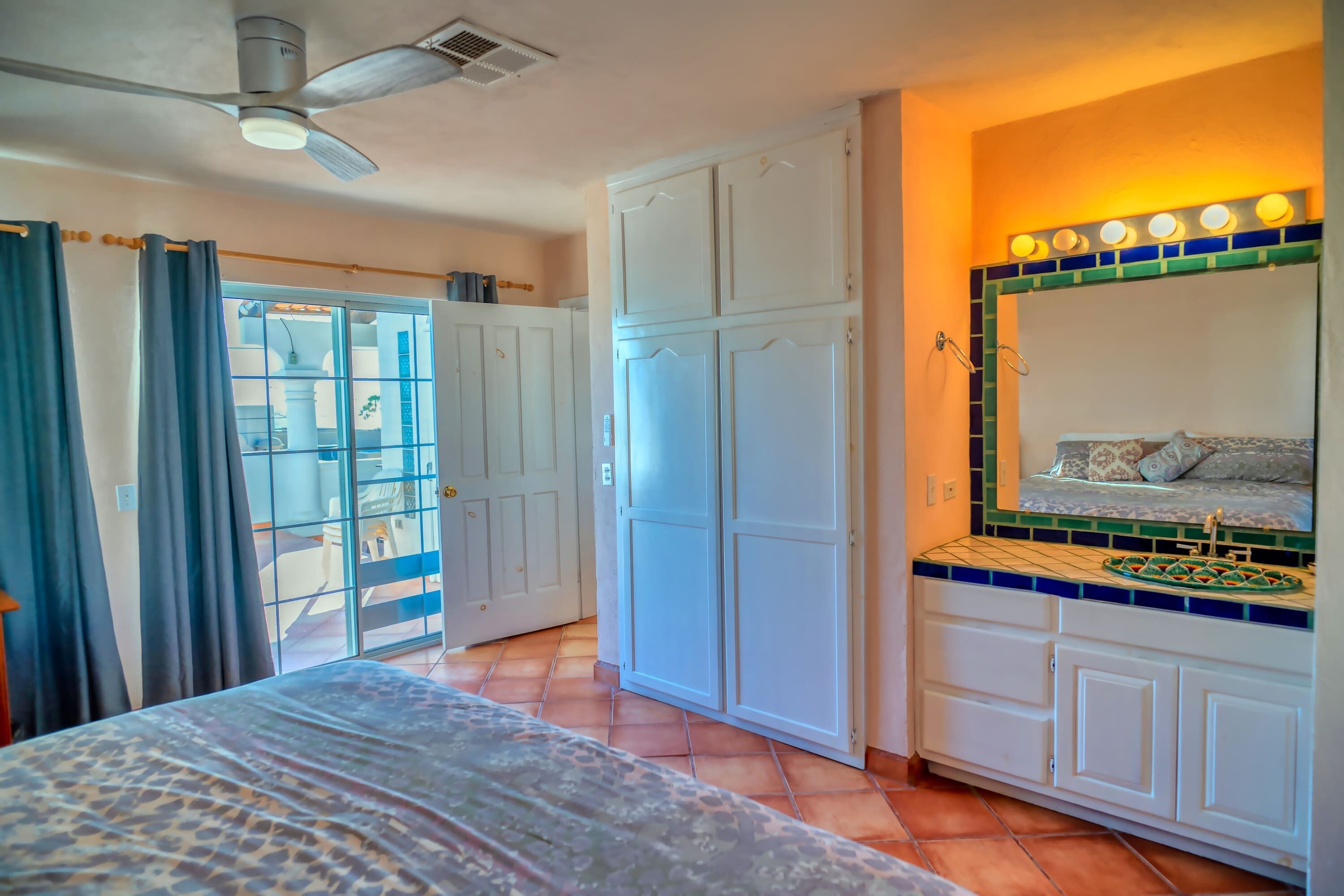 A bedroom with a bed, a ceiling fan, a wardrobe, and a bathroom vanity with a mirror.