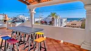 A terrace with a table and stools, a view of the sea, and a tiled roof.
