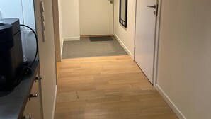 Un pasillo con suelo de madera, una puerta blanca al final y un espejo con marco negro en la pared.