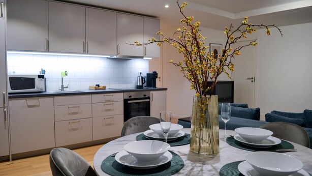 Una cocina moderna con armarios blancos, un microondas y una cafetera. Hay una mesa de comedor con platos y un florero con flores.
