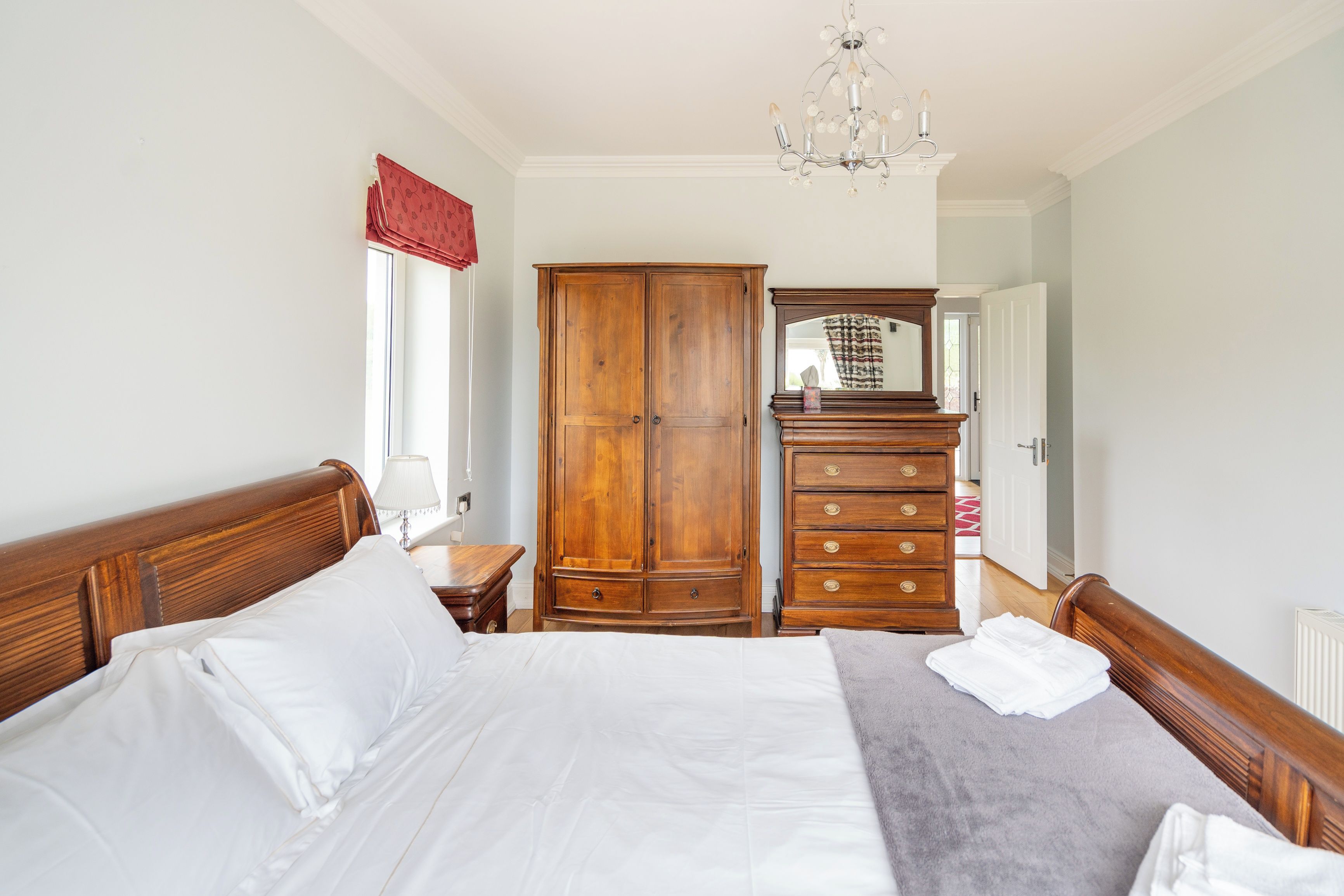 A bedroom with a large bed, wooden wardrobe, dresser, and a chandelier.