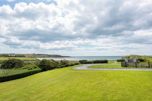 A coastal landscape with a grassy field, a winding road, and a small building near the water.