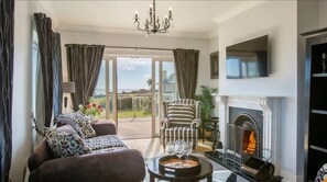 A living room with a fireplace, a sofa set, and a view through a glass door to the outdoors. - Waterford Villa 5 Bed Beach Retreat (Ardmore)