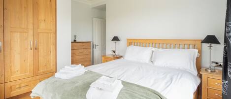 A bedroom with a large wooden wardrobe, a bed with white linens, two bedside tables with lamps, and a green throw blanket on the bed.