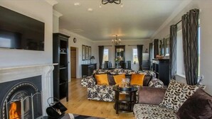A living room with a fireplace, patterned sofa, and a dining area with a chandelier. - Waterford Villa - 5 Bed - Sleeps 10 - Parking (Ardmore)