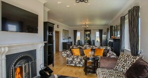 A living room with a fireplace, patterned sofa, and a dining area with a chandelier. - Waterford Villa - 5 Bed - Sleeps 10 - Parking (Ardmore)