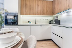 Une cuisine moderne avec des meubles blancs, un four encastré, un four à micro-ondes et un évier.