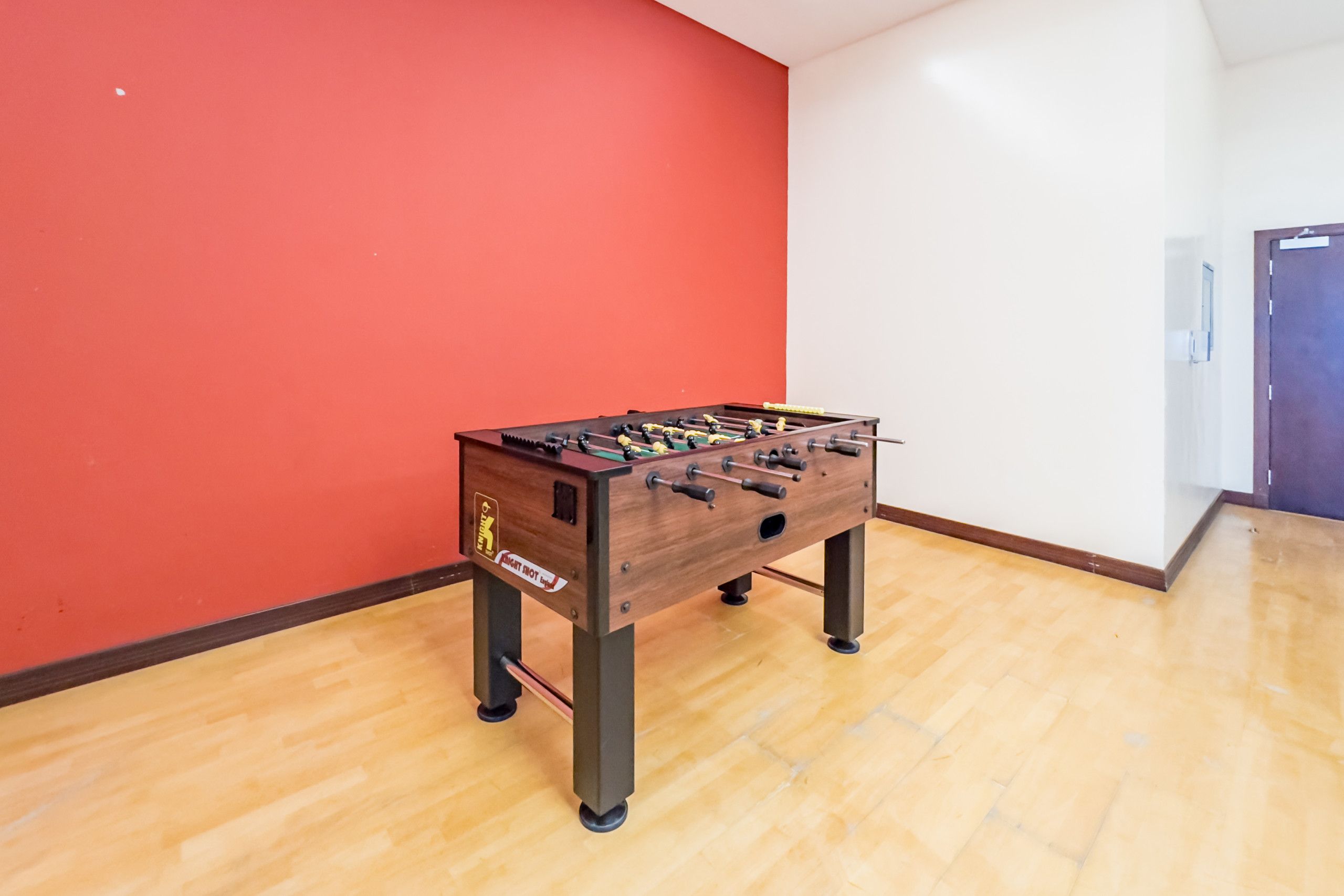 Ein Zimmer mit Holzboden, roter Wand und einem Kicker.