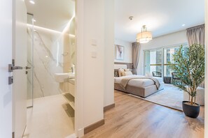 A modern bedroom with a glass shower, a large bed, and a potted plant. - Renovated Unit w/ Skyscraper Views Close to Beach, Elite Residence,Dubai Marina (Dubai)