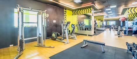 Ett gym med olika typer av träningsutrustning, inklusive styrketräningsmaskiner och lösa vikter, placerat på ett trägolv med svarta mattor.