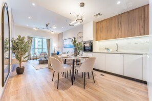 A modern kitchen with wooden cabinets, a dining area with a round table and chairs, and a large window with curtains. - Renovated Unit w/ Skyscraper Views Close to Beach, Elite Residence,Dubai Marina (Dubai)