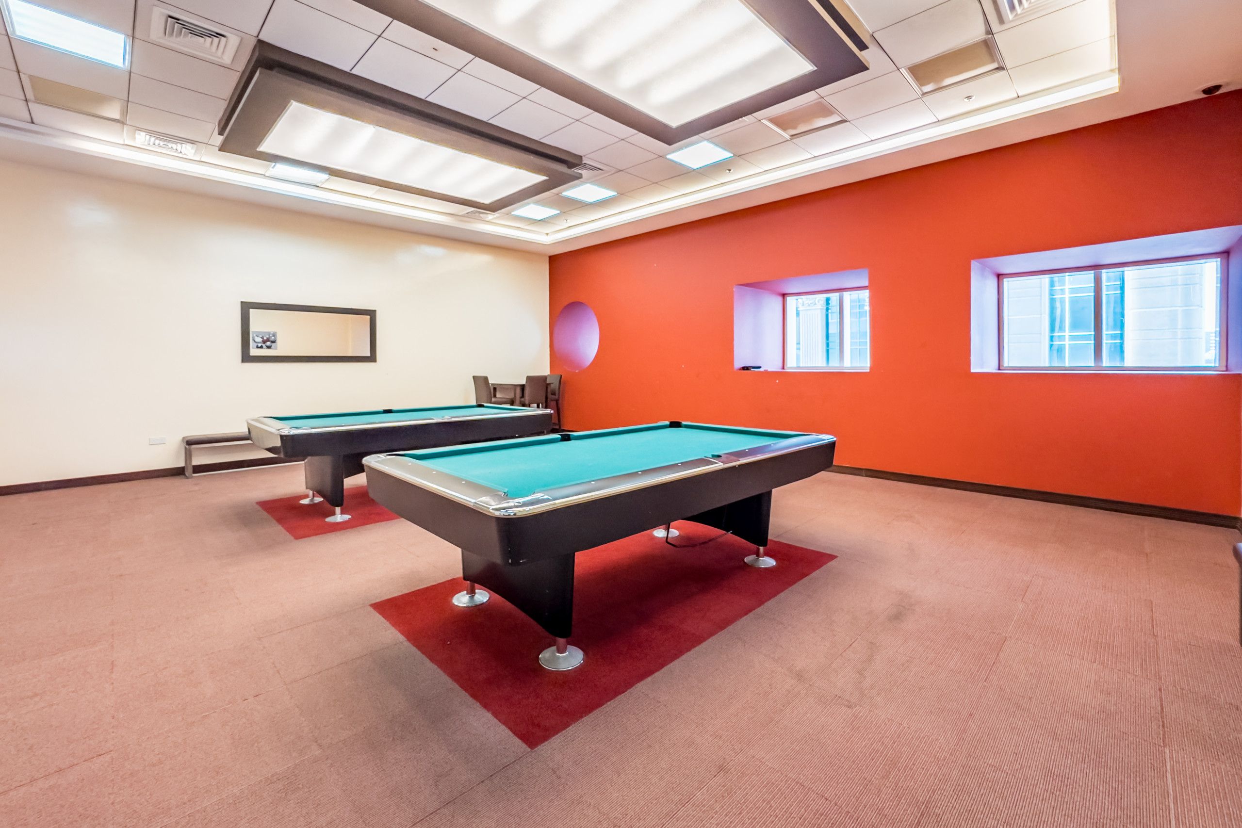 A pool table room with two pool tables, a red carpet, and a ceiling with recessed lighting.