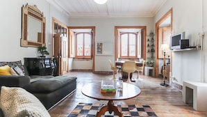 Una sala de estar con un sofá, una mesa de centro con libros, un televisor y un comedor con sillas y una mesa.