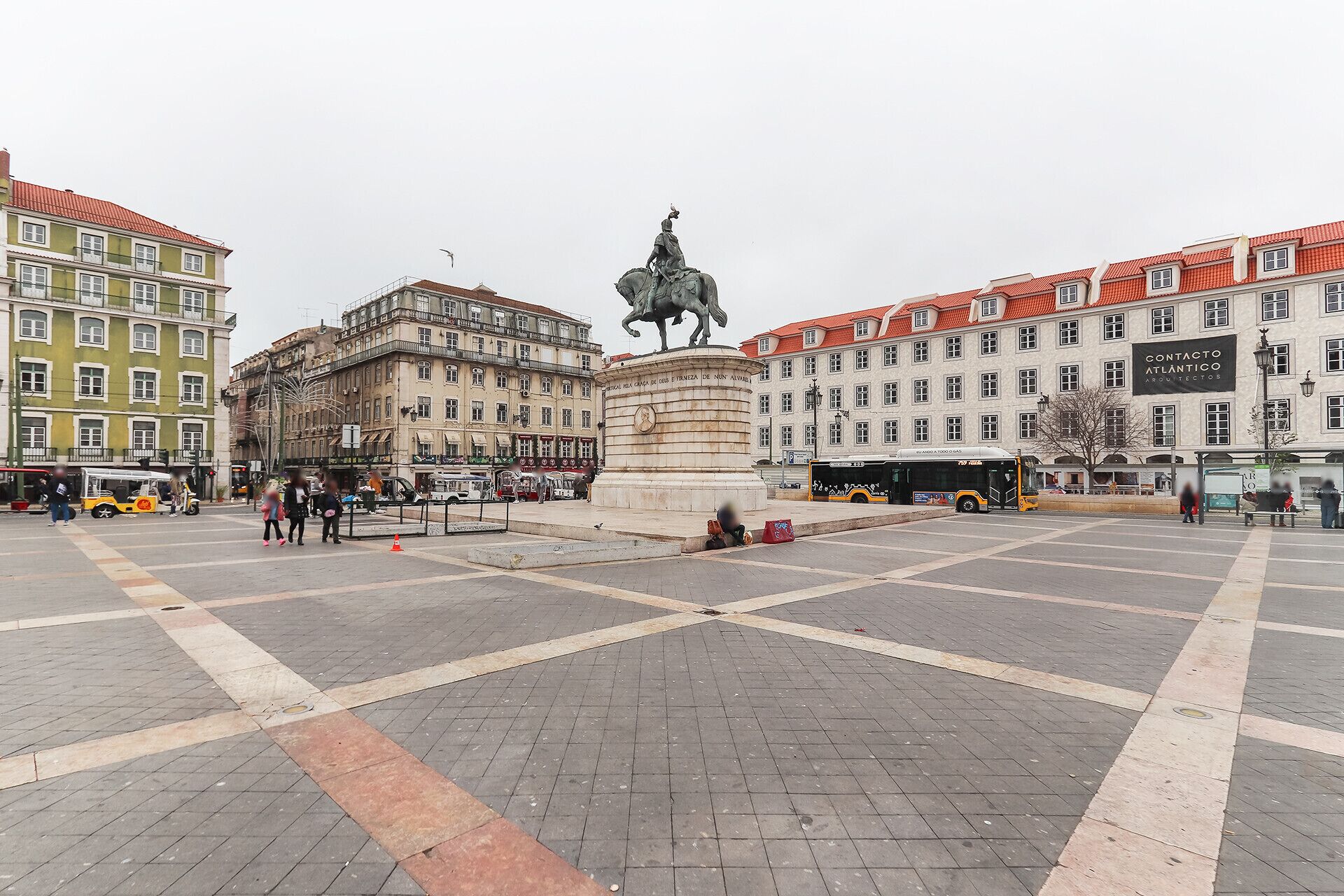 Una plaza pública con una estatua, edificios con tejados rojos y un autobús.