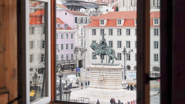 Vista de una plaza urbana con una estatua ecuestre, rodeada de edificios históricos con tejados rojos.
