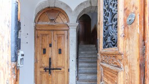 Una puerta de madera con un cerrojo metálico y una placa de metal, que da acceso a una escalera con escalones de piedra.