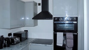 Eine kleine Küche mit weißen Schränken, einer schwarzen Dunstabzugshaube, einem eingebauten Backofen, einer Mikrowelle und einem Toaster.