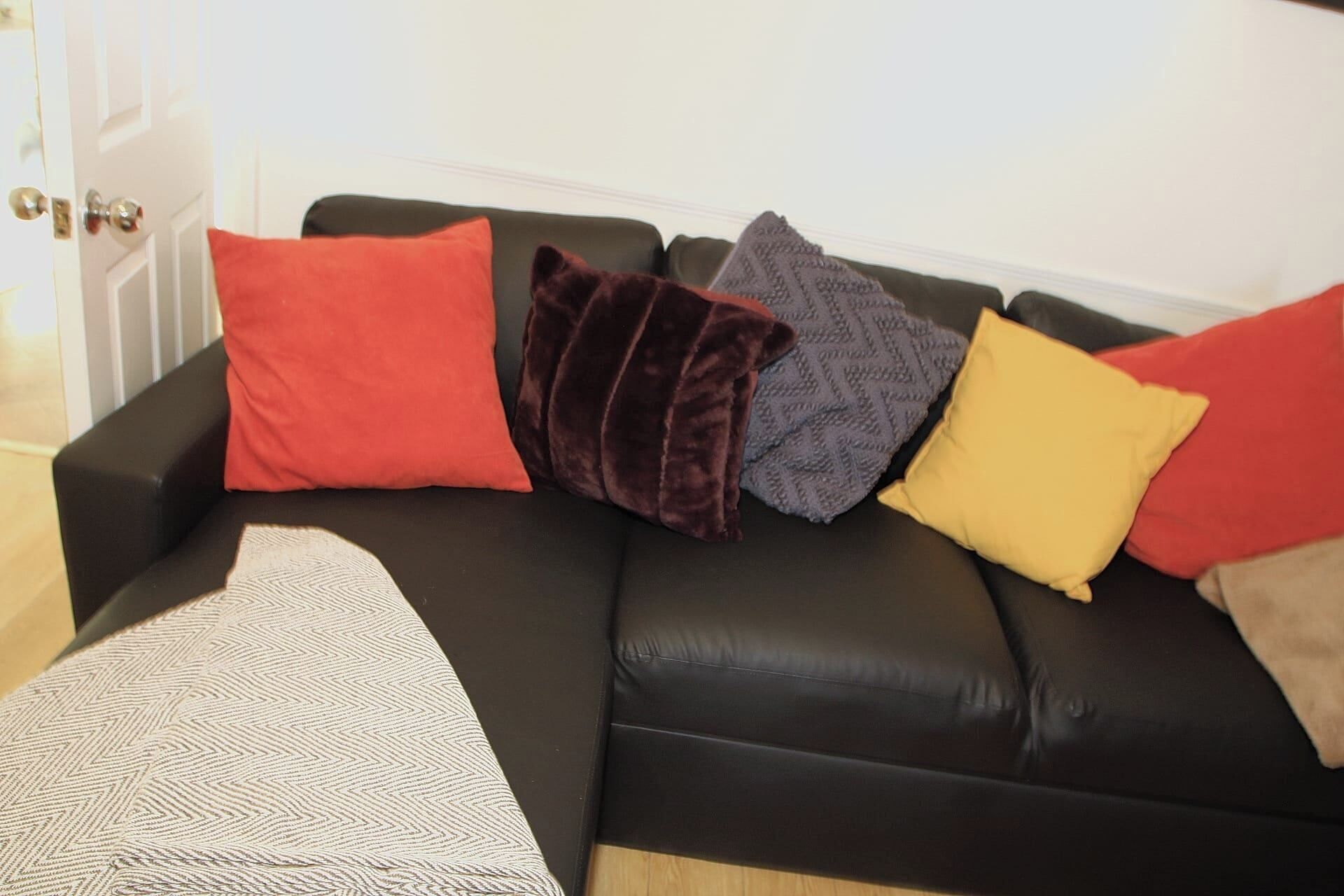 A black leather sofa with four cushions in red, brown, grey, and yellow.