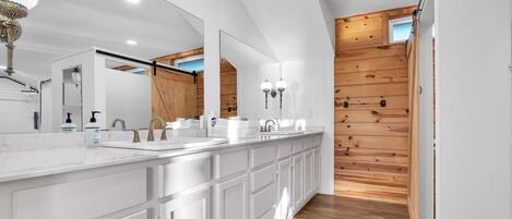 A modern bathroom with a large mirror, white cabinetry, and a wooden accent wall.