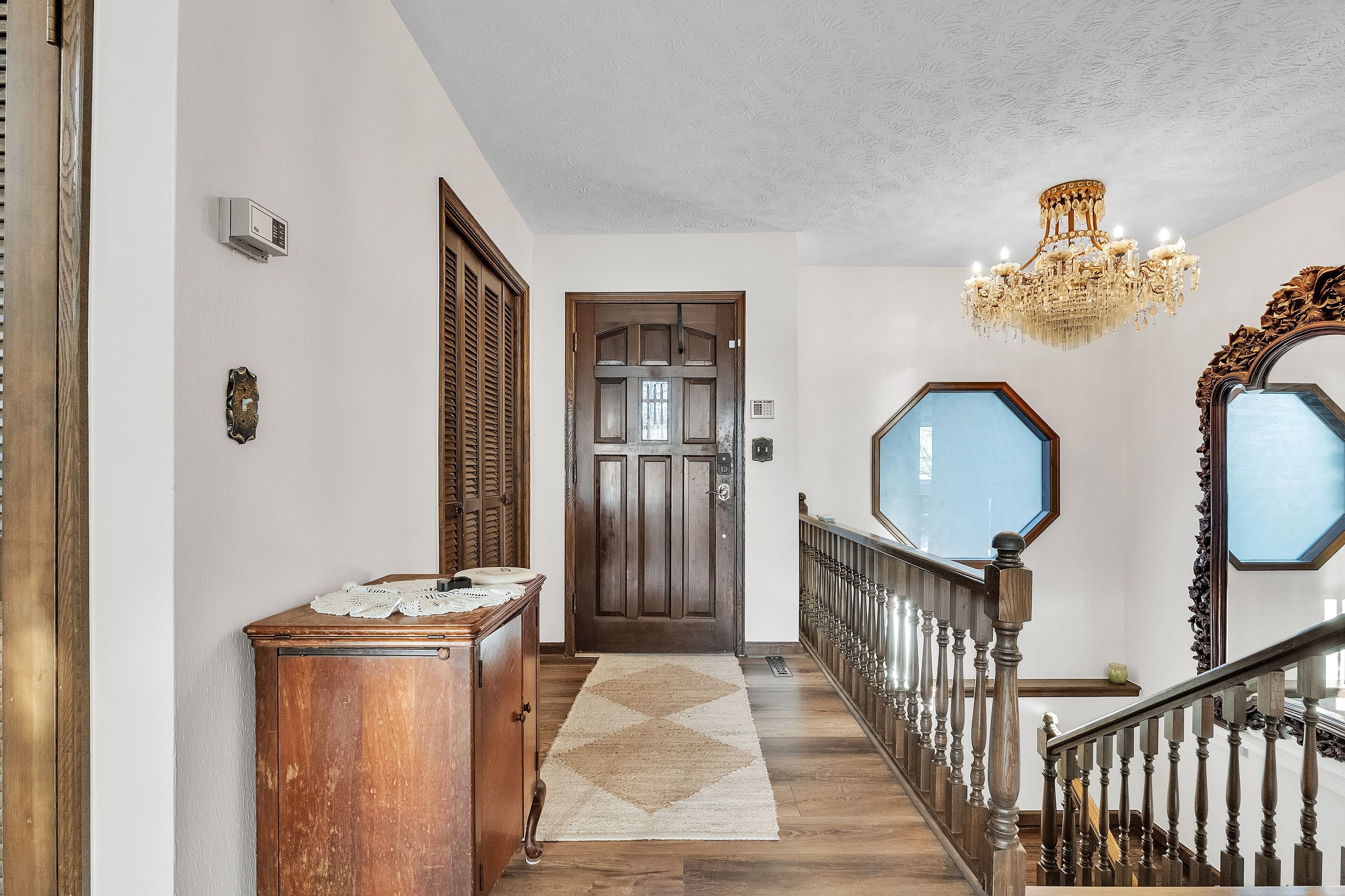 A hallway with a wooden door, a chandelier, and a mirror.
