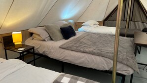 A tented accommodation with a bed, pillows, a lamp, and a table. - Cozy Hot Tent With Log Burner & Hot Tub Right Tent (Gaerwen)