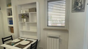 A dining area with a white table and chairs, a window with blinds, and a radiator below the window. - Little Aventino B&B - Charming bed & breakfast with AC/WiFi in the heart of Rome (Rome)