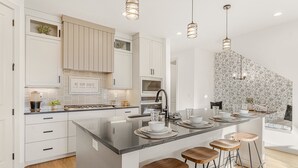 A modern kitchen with white cabinetry, a large island with stools, and pendant lighting. - Always An Adventure 4 Bedroom Townhouse (St. George)