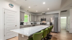 Una cocina moderna con una isla de mármol, taburetes de bar verdes, electrodomésticos de acero inoxidable y piso de madera clara.
