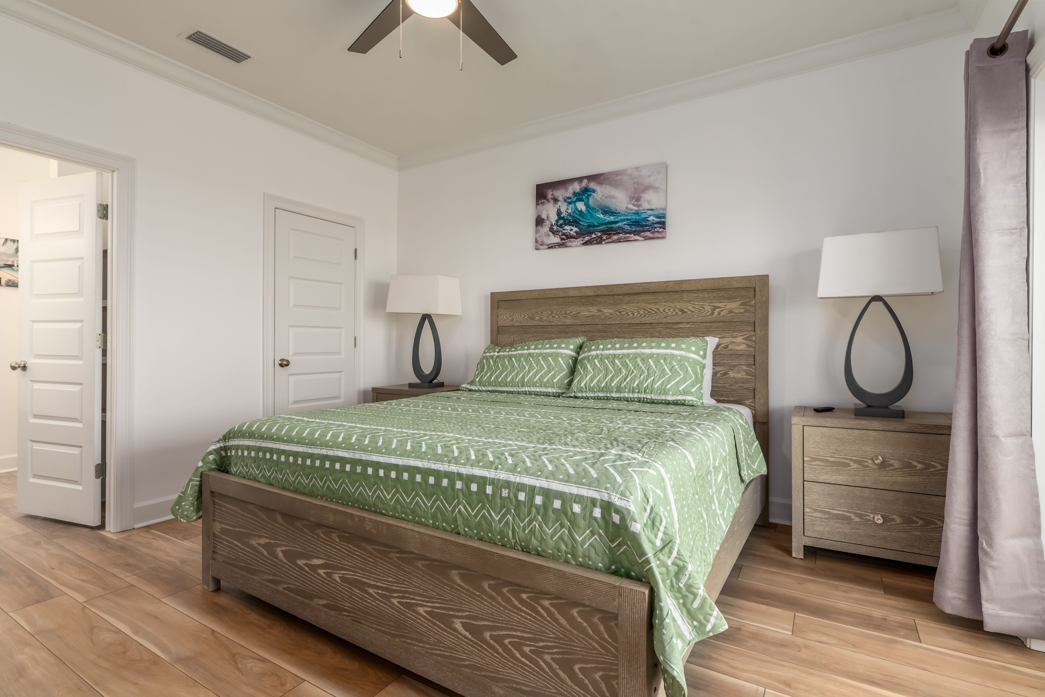 Una camera da letto con un letto in legno, biancheria da letto verde con motivi, due abat-jour, un comodino e un quadro appeso al muro.