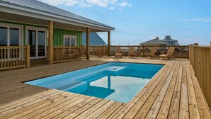 Una terraza de madera con piscina, mobiliario exterior y un edificio con fachada verde.