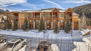 A multi-story lodge with balconies, surrounded by snow-covered ground and trees, featuring a clear sky. - 5959 Hidden River Lodge 2 Bedroom Condo (Keystone)