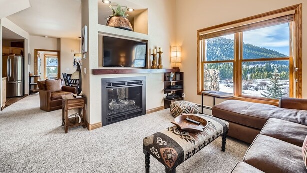 A cozy living room with a fireplace, a large window with a scenic view, and a comfortable seating area. - 5959 Hidden River Lodge 2 Bedroom Condo (Keystone)