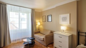 Hotellihuone, jossa on sohva, pieni pöytä, lamppu, sänky ja lipasto.