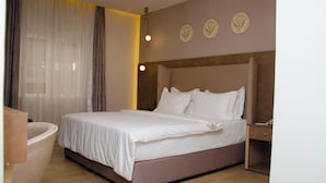 Una habitación de hotel moderna con una cama grande, una mesita de noche, una silla y un ventanal con cortinas.