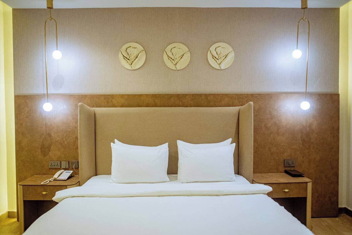 A hotel room with a large bed, two bedside tables, a wall-mounted phone, and three wall sconces.