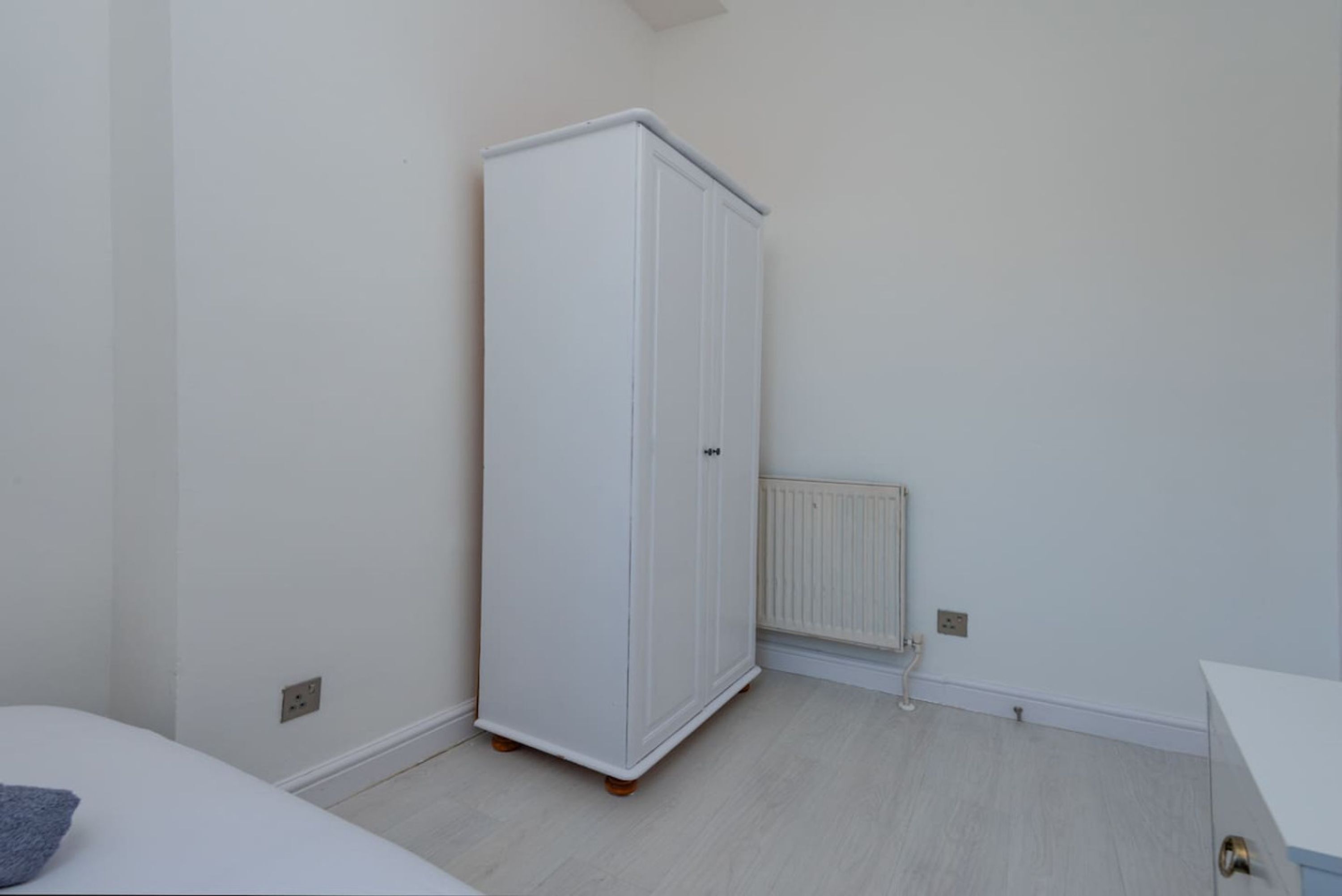 Una habitación con armario blanco, radiador y cama blanca.