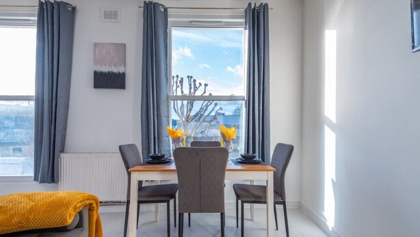 A modern dining area with a table set for four, a sofa, and a view of the city through large windows.