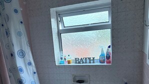 A bathroom with a bathtub, a window with toiletries, a shower curtain, and a towel rack. - 3 Bed House - Sleeps 6 - Parking - Wifi (Leicester)