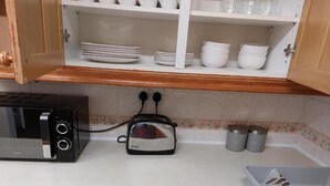 A kitchenette with a microwave, toaster, and cabinets containing dishes and cups. - 3 Bed House - Sleeps 6 - Parking - Wifi (Leicester)