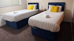 Two twin beds with blue headboards and white bedding, each with a yellow pillow and a rolled towel. - 3 Bed House - Sleeps 6 - Parking - Wifi (Leicester)