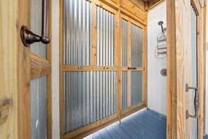 A wooden door with a metal mesh screen, a wooden floor, and a metal showerhead.