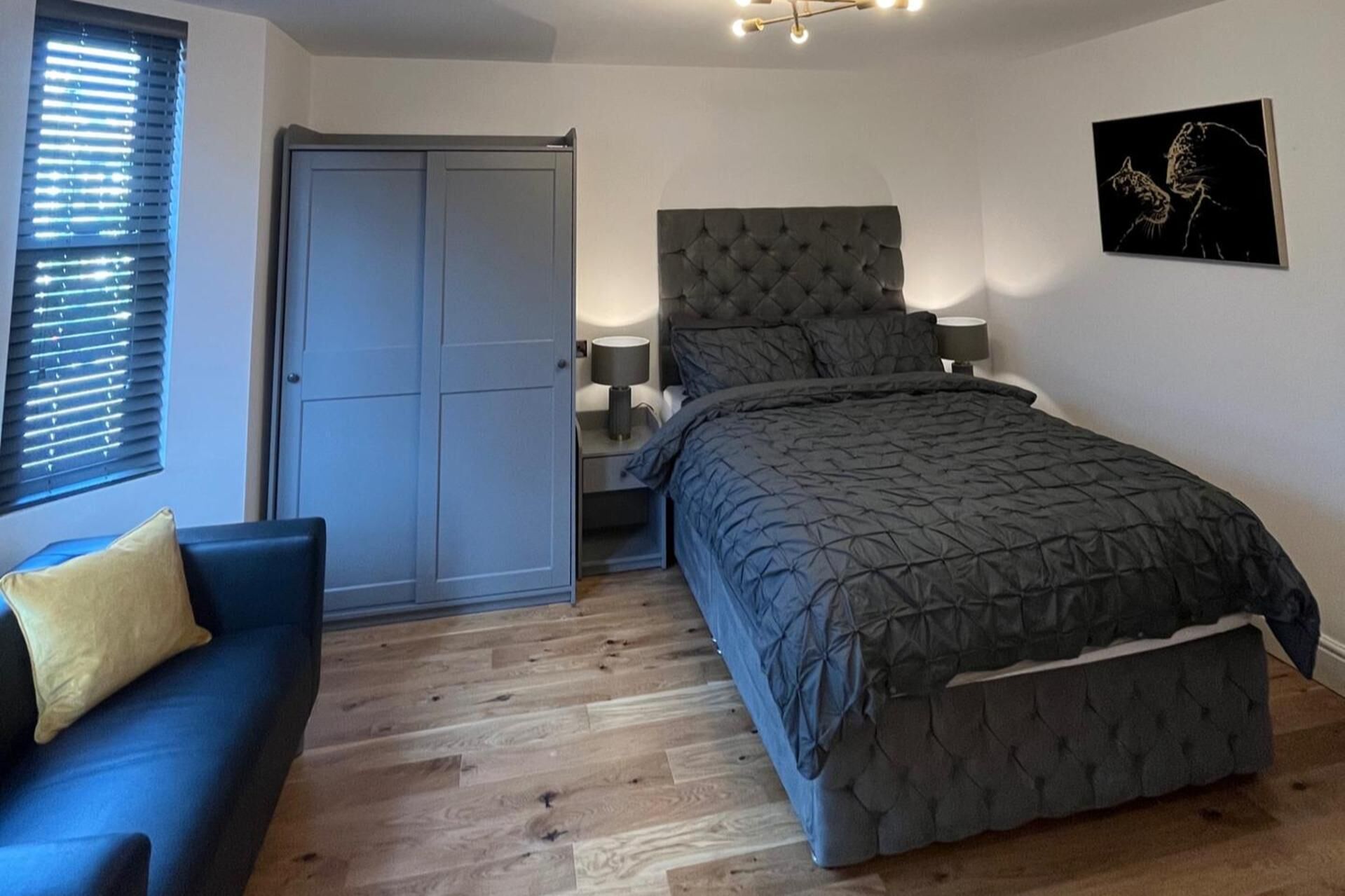 A bedroom with a bed, a nightstand, a lamp, a blue sofa, and a door.