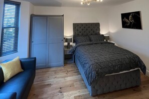 A bedroom with a bed, a nightstand, a lamp, a blue sofa, and a door. - Cozy London Apartment , 2 Minutes to Tube! (London)