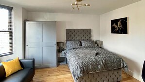 A bedroom with a bed, a nightstand, a dresser, a sofa, and a window with blinds. - Cozy London Apartment , 2 Minutes to Tube! (London)