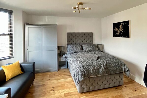 A bedroom with a bed, a nightstand, a dresser, a sofa, and a window with blinds. - Cozy London Apartment , 2 Minutes to Tube! (London)