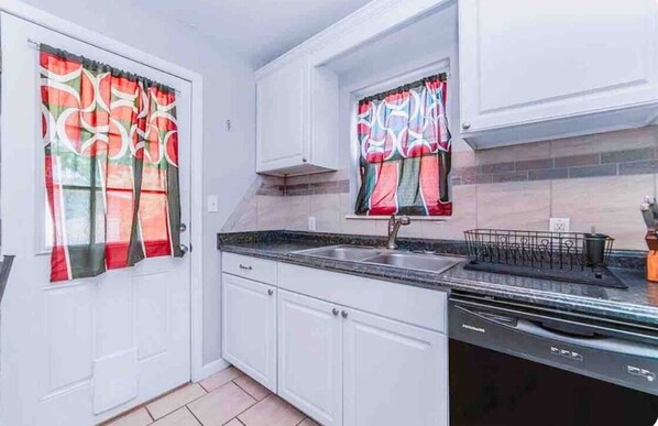 A kitchen with white cabinets, a black countertop, a sink, and a dish rack. - Pet friendly 3 bedroom house in central Okc (Oklahoma City)
