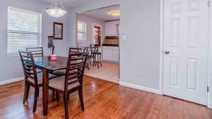 Un coin repas avec une table et des chaises en bois, un lustre et une vue sur la cuisine.