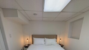 A neatly made bed with white linens and two towels, a headboard, bedside lamps, and a window with blinds. - Comfy 2-bedroom apartment with AC, WiFi in Oak Park (Oak Park)