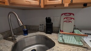 A kitchen with wooden cabinets, a stainless steel sink, a faucet, a dish rack, and a knife block. - Comfy 2-bedroom apartment with AC, WiFi in Oak Park (Oak Park)