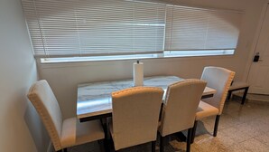 A dining area with a marble table and four upholstered chairs, a window with blinds, and a tiled floor. - Comfy 2-bedroom apartment with AC, WiFi in Oak Park (Oak Park)